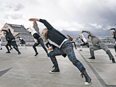 Tänzer:innen stehen auf einem Parkdeck und beugen sich synchron nach link